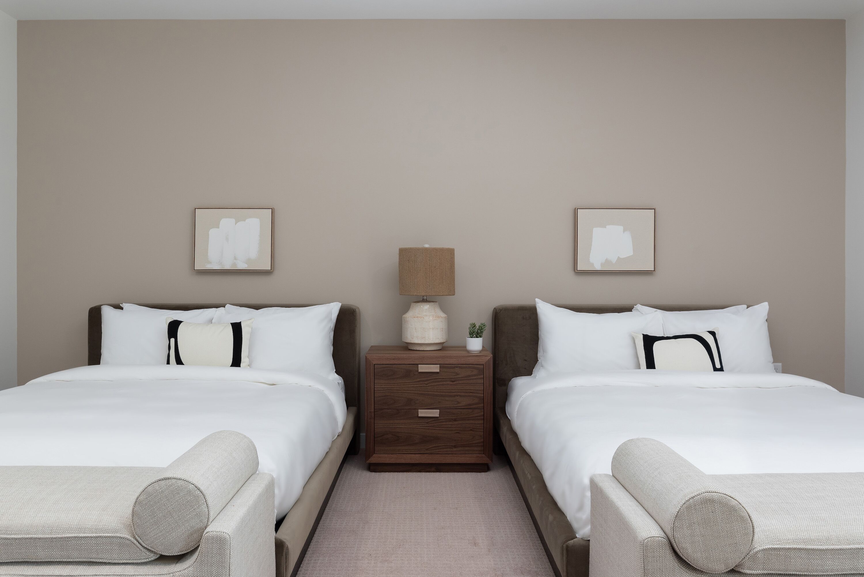 A hotel room with two beds, a nightstand with a lamp, and a small potted plant.