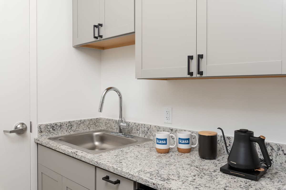 Una cocina con encimera de granito, pileta de acero inoxidable y cafetera negra.