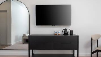 Een moderne kamer met een zwarte televisie aan de muur, een zwart console tafeltje met twee bekers en een koffiezetapparaat, en een stoel.
