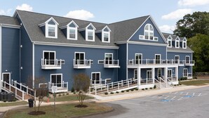 A multi-story building with a blue exterior and white trim, featuring balconies and a covered entrance area.