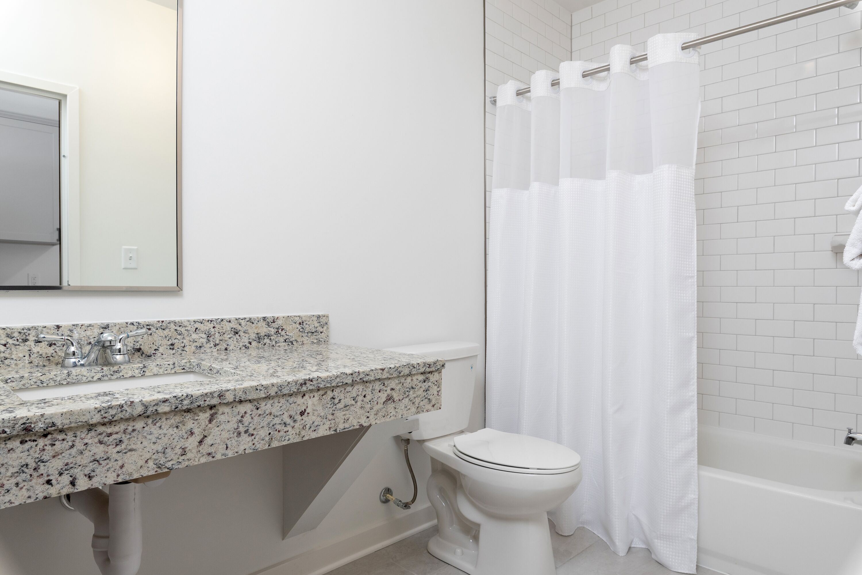 A bathroom with a white toilet, a granite countertop sink, and a shower with a white curtain.