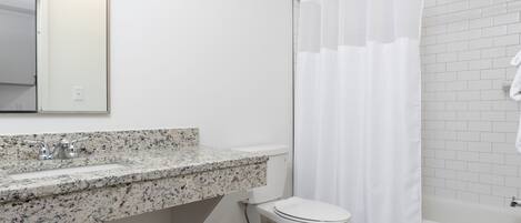 A bathroom with a white toilet, a granite countertop sink, and a shower with a white curtain.