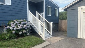 Ein Haus mit blauer Fassade, einer weißen Treppe und einem Garten mit Hortensienblüten.