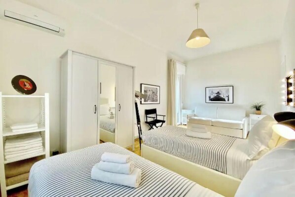 A hotel room with two beds, a wardrobe, a desk, and a mirror.