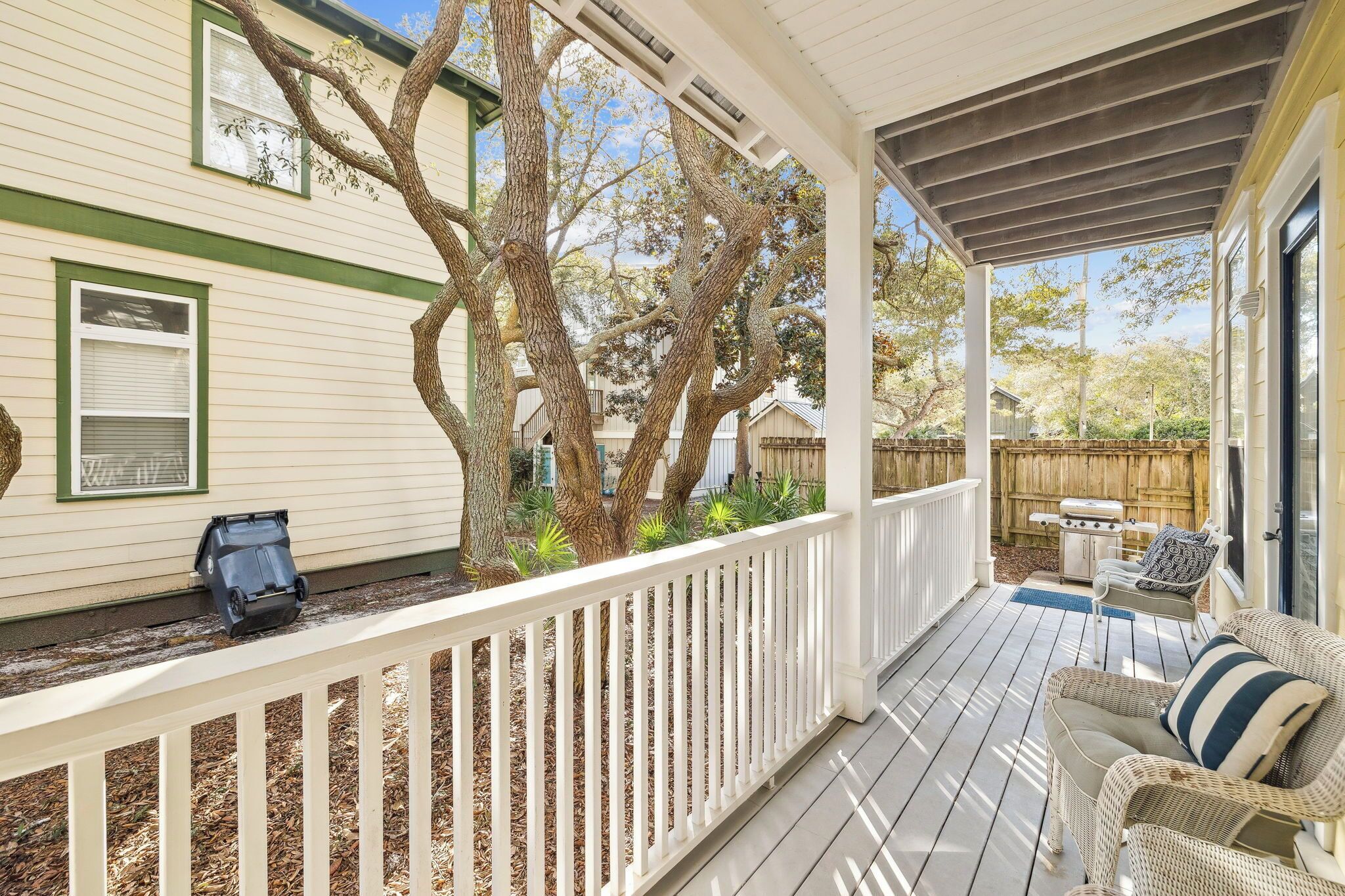 A covered porch with a white railing, outdoor furniture, and a tree.