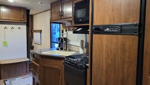 A compact kitchen with wooden cabinets, a built-in microwave, a refrigerator, and a gas stove. - Camp in style with AC/heat, WIFI, on Main Street, 1 block from Joni's beach (La Pointe)