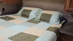 A compact RV interior with a bed featuring a patchwork quilt and a headboard with built-in lighting. - Camp in style with AC/heat, WIFI, on Main Street, 1 block from Joni's beach (La Pointe)