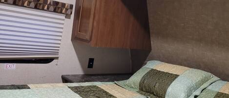 A bedroom with a bed, a wooden cabinet, and a window with blinds.