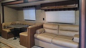 A compact RV interior with a dining table, two cushioned seating areas, and built-in cabinets. - Camp in style with AC/heat, WIFI, on Main Street, 1 block from Joni's beach (La Pointe)