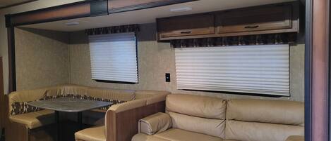 A compact RV interior with a dining table, two cushioned seating areas, and built-in cabinets.