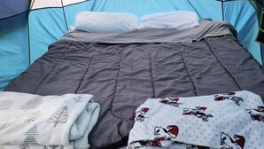 A tent with a bed inside, featuring a grey and white quilt and a blanket with a pattern. - Peaceful camp with breathtaking views (Westmore)