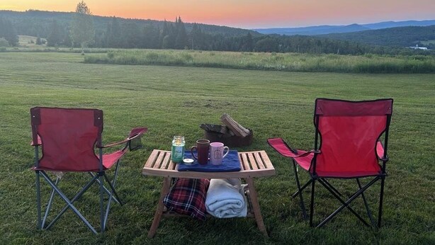 An outdoor seating area with two red chairs and a table set for two, overlooking a grassy field and distant hills. - Peaceful camp with breathtaking views (Westmore)