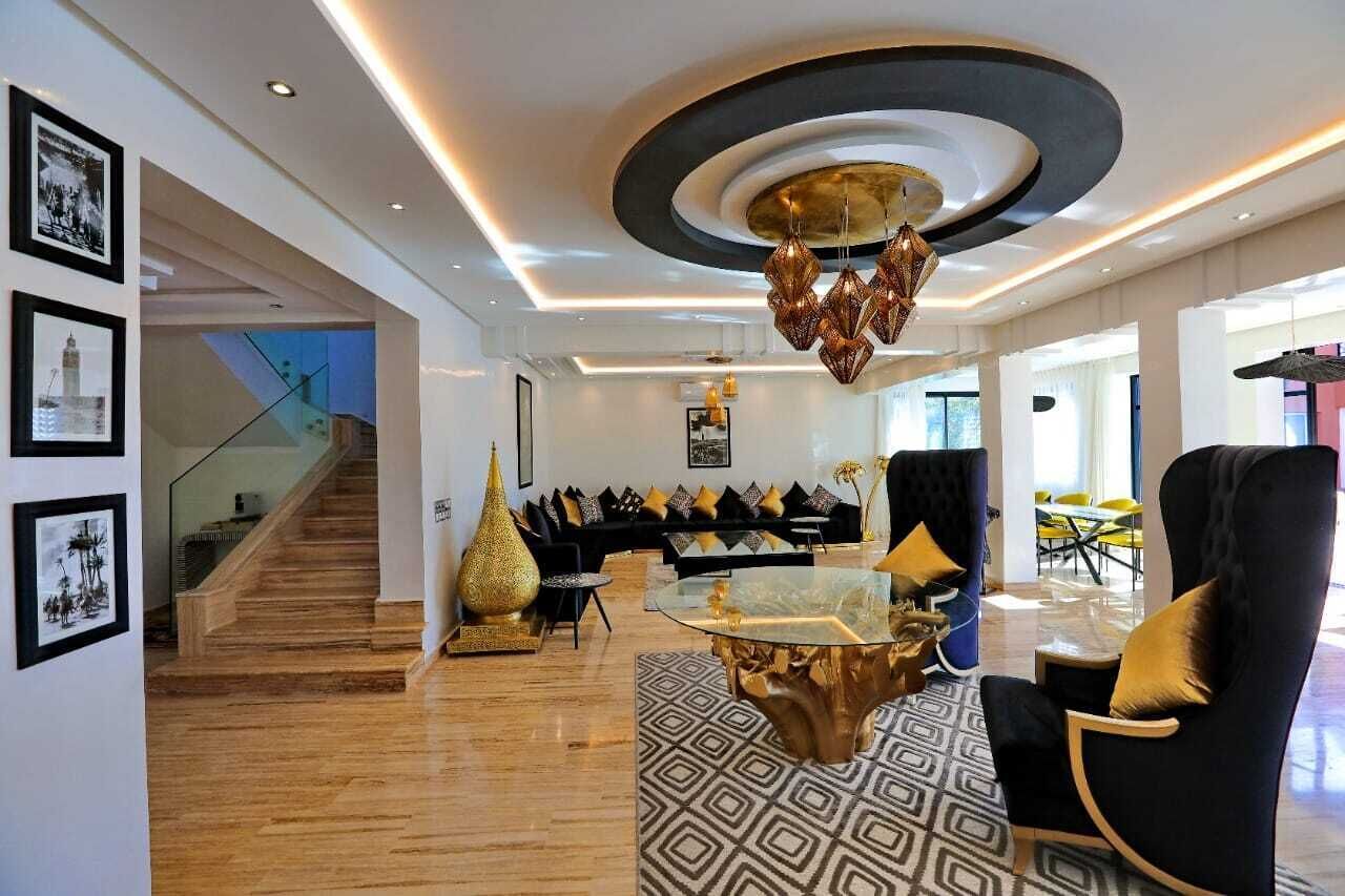 Un salon moderne avec une table basse en verre, des canapés noirs et dorés, et un design de plafond original.
