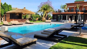 Une piscine avec des chaises longues, une structure à toit de chaume et un bâtiment doté d’un balcon.