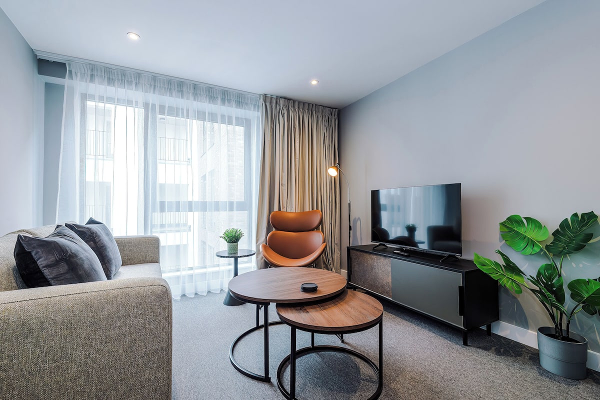 Una sala de estar moderna con un sofá, una mesa redonda de centro, un televisor y una planta en maceta.