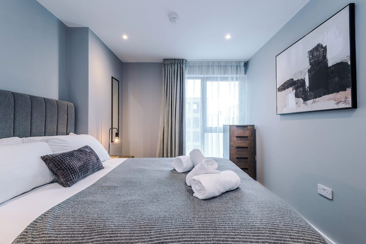 Una habitación de hotel moderna con una cama grande, una mesita de noche, un armario y una ventana con cortinas.