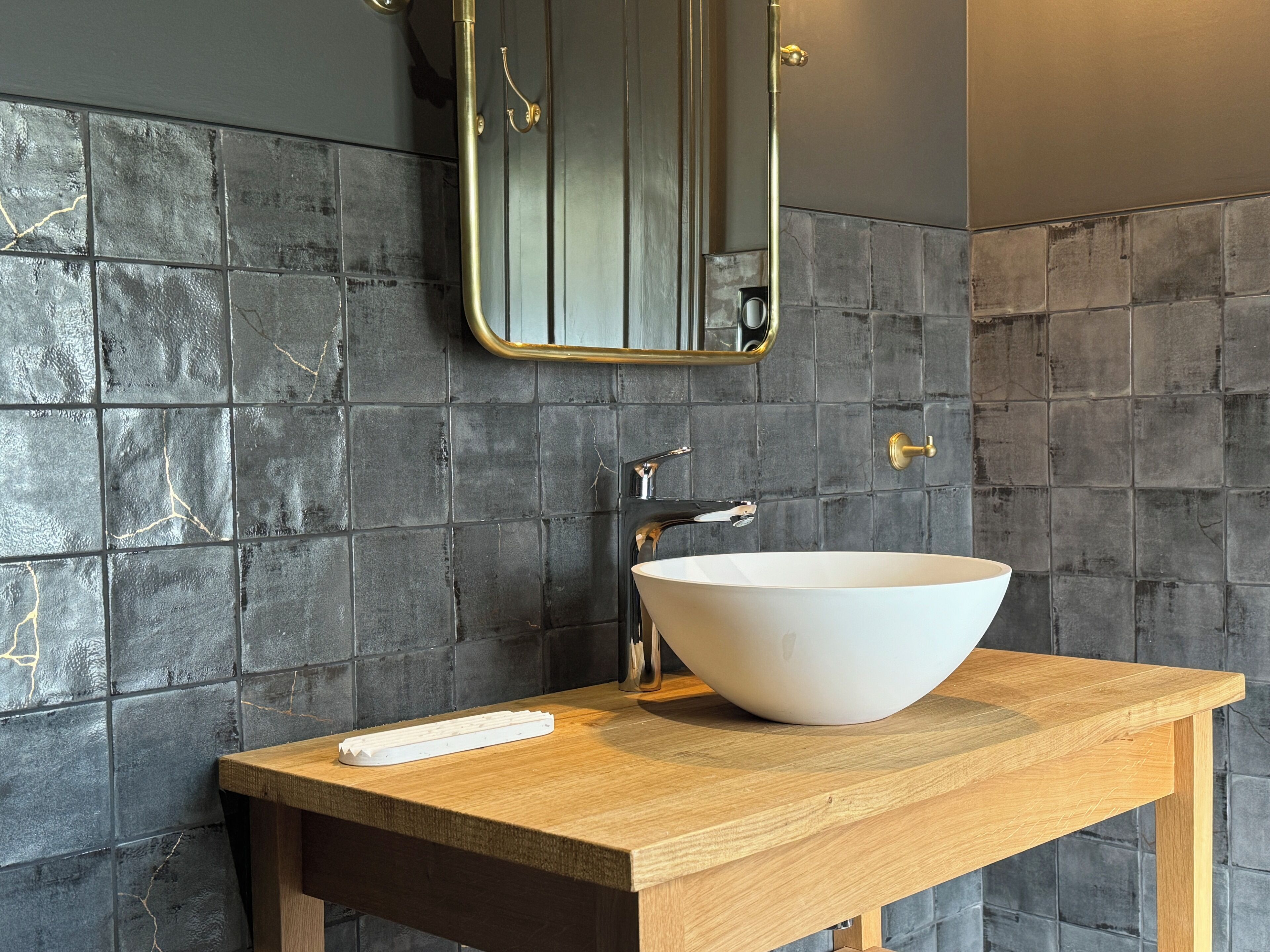 A bathroom with a large white vessel sink, a wooden vanity, and a mirror with a gold frame.