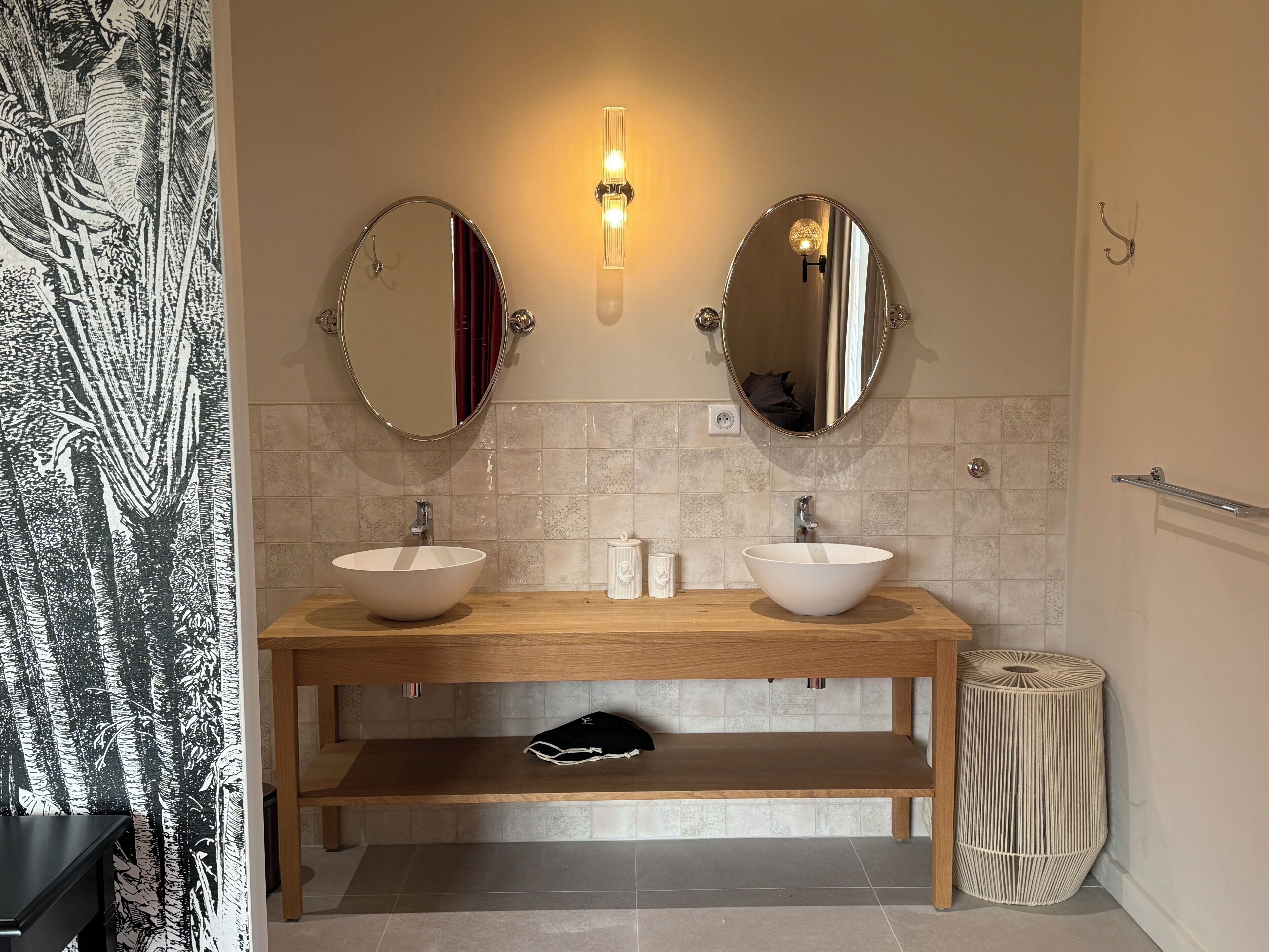 A bathroom with two sinks, a bench, a trash can, and a wall-mounted light fixture.