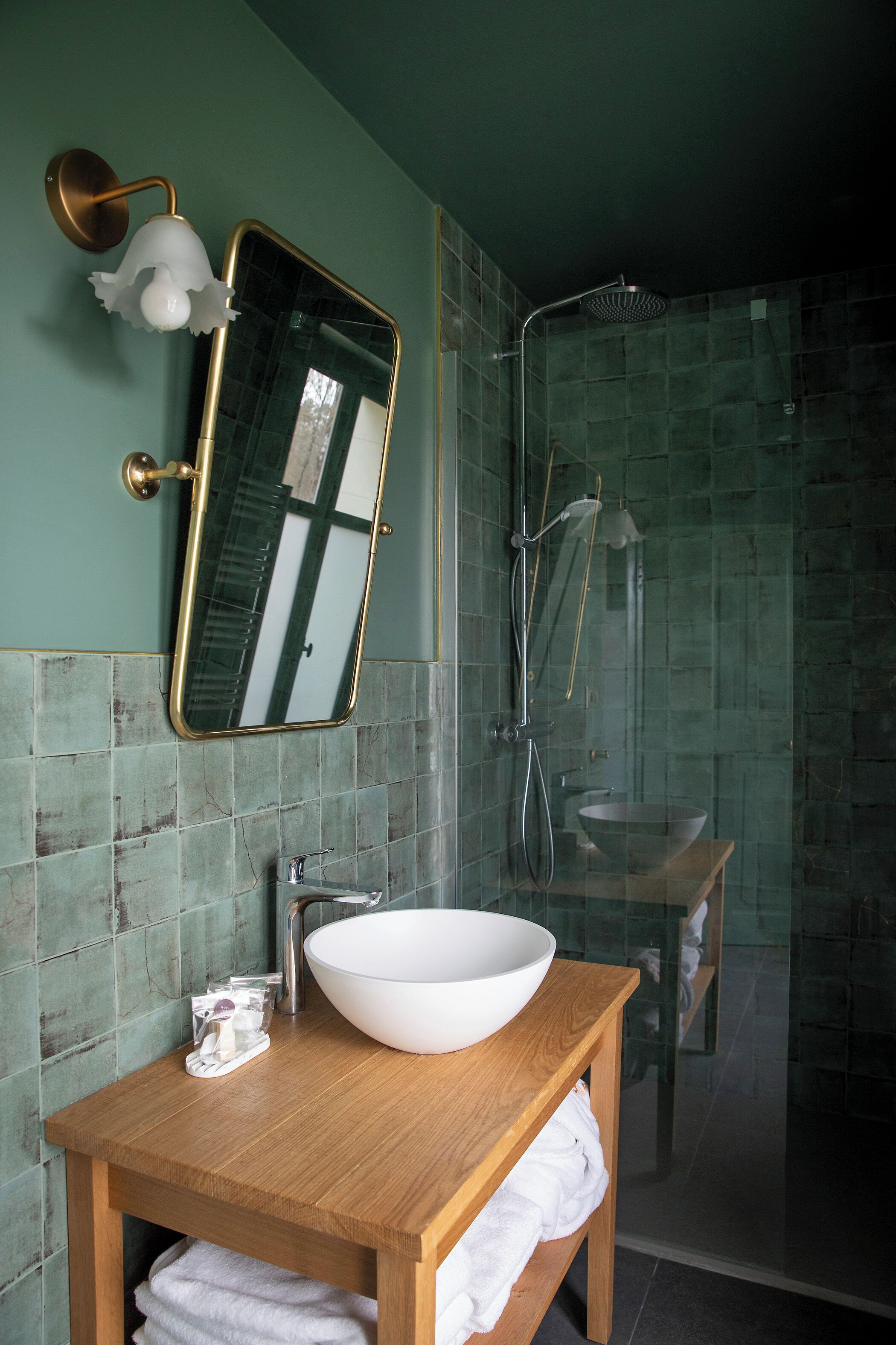 Une salle de bain avec un meuble-lavabo en bois, un lavabo blanc, un miroir et une douche séparée par une paroi de verre.