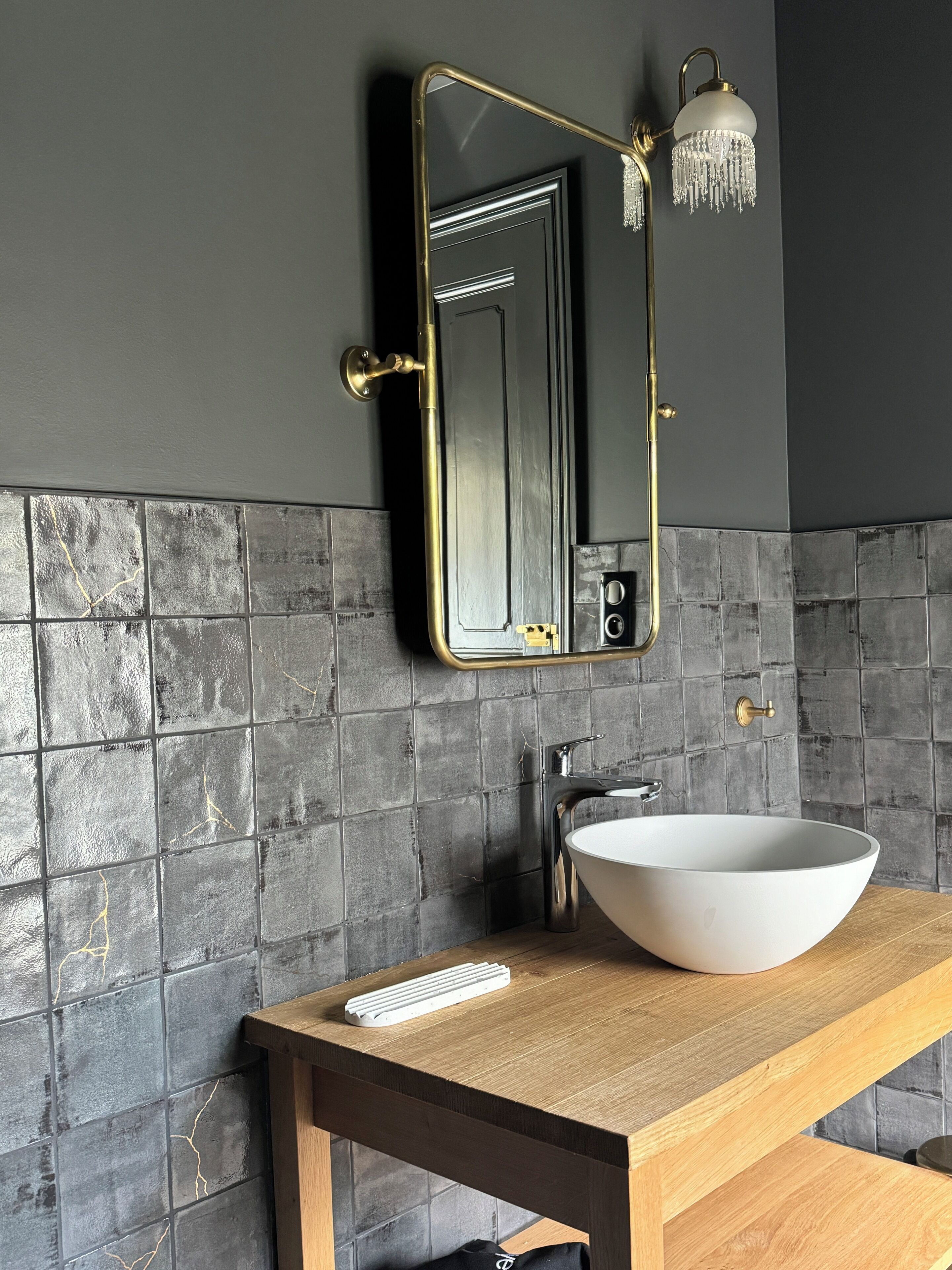 A bathroom with a large white sink, a gold-framed mirror, and a wall-mounted light fixture.