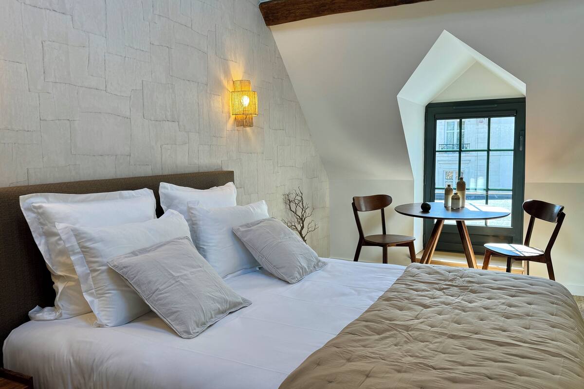 Een slaapkamer met een groot bed, een wandlamp en uitzicht buiten door een raam.