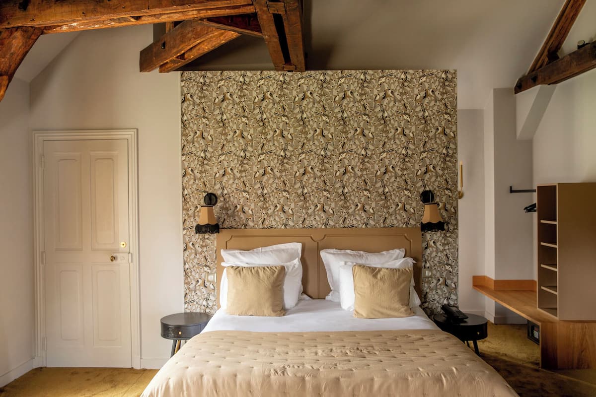 Een slaapkamer met een groot bed, houten balken, een behang met patroon en een kledingkast.