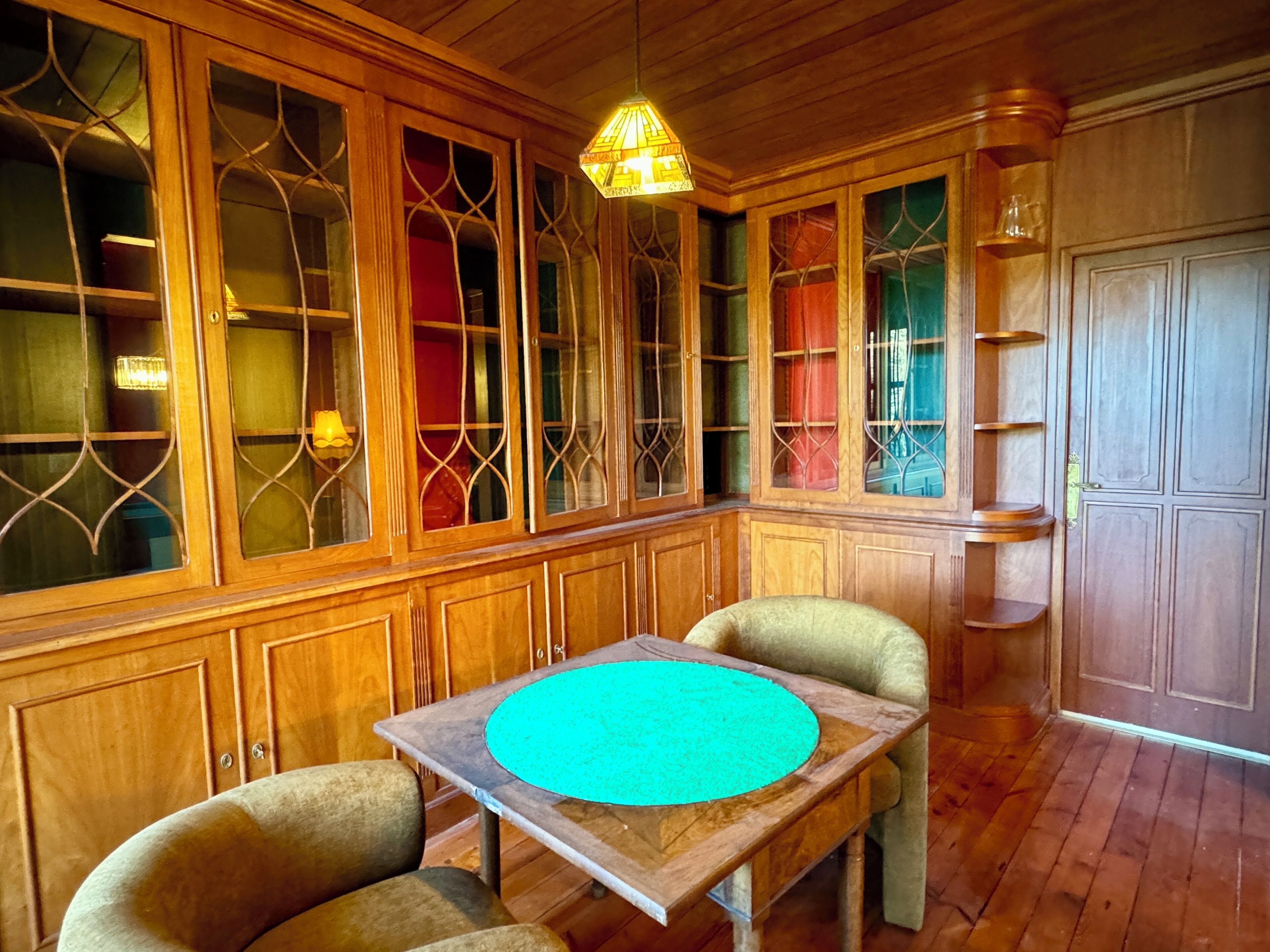 Quarto com paredes revestidas de madeira, uma mesa de madeira com tampo azul-turquesa e duas cadeiras.