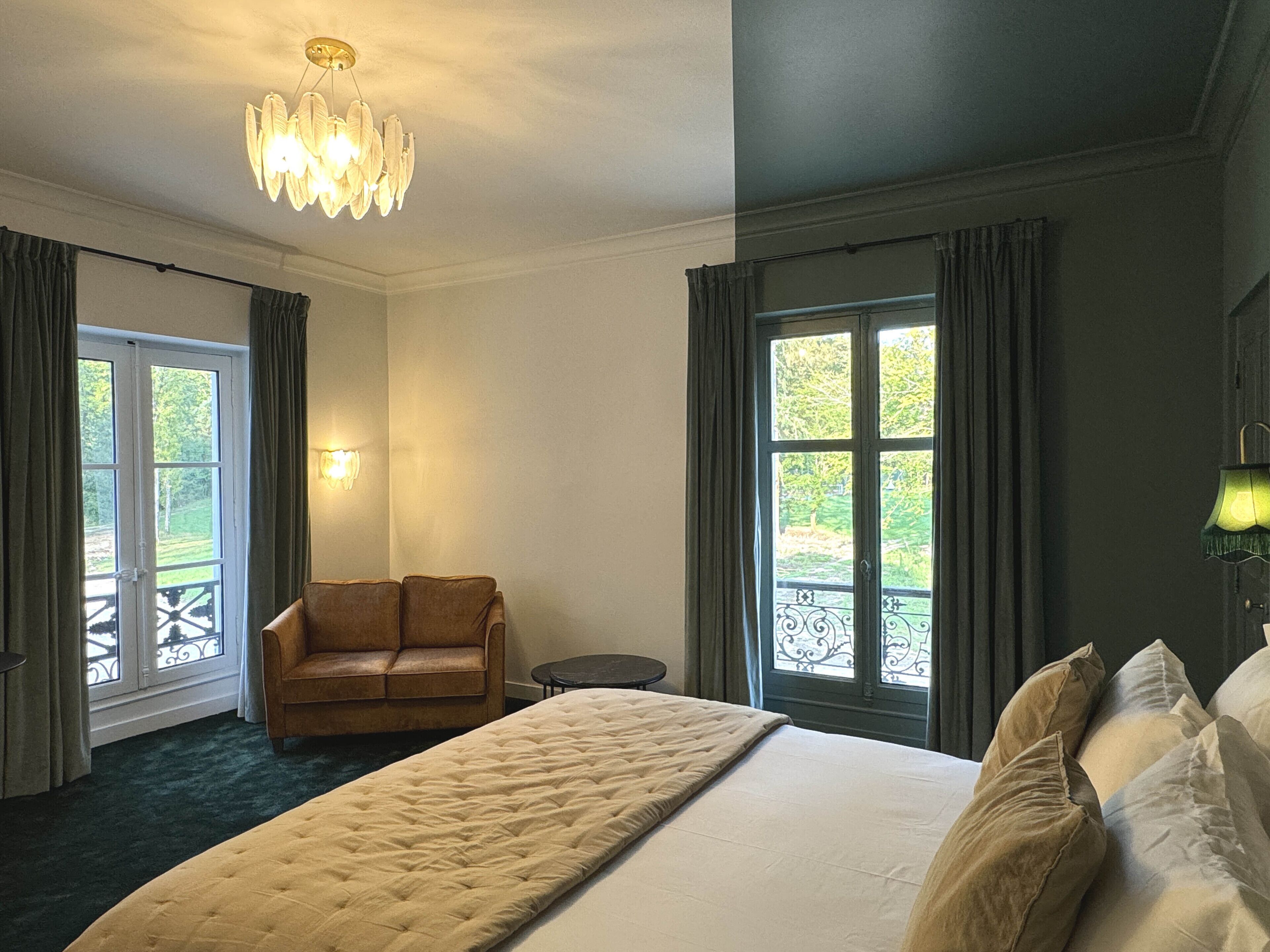 A hotel room with a large bed, a sofa, a small table, and a chandelier.