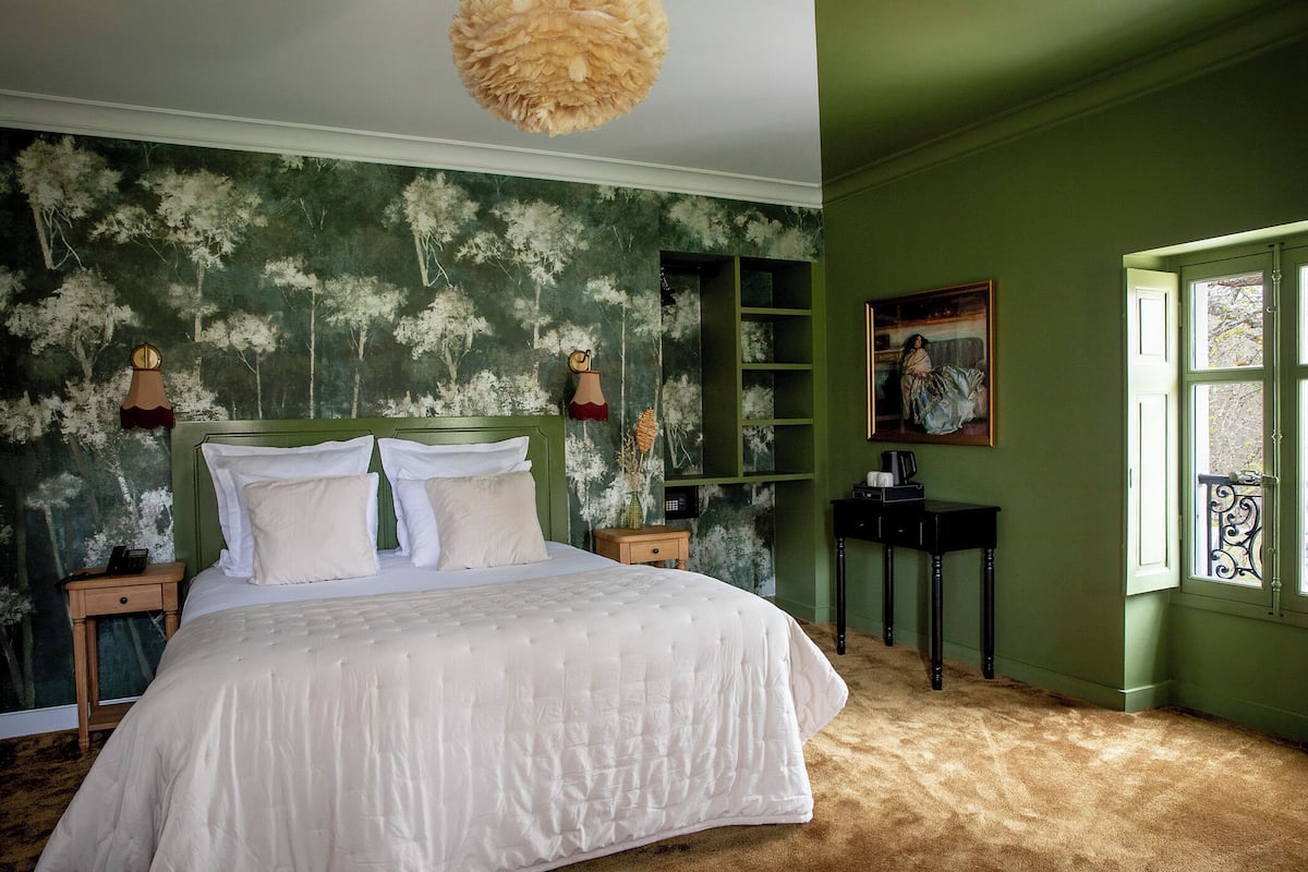 Een slaapkamer met een groot bed, groene wanden, een raam met uitzicht en een schilderij aan de muur.
