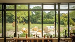 A room with large windows, wooden furniture, and a view of an outdoor garden. - Les Hayes en Sologne (Fontaines-en-Sologne)