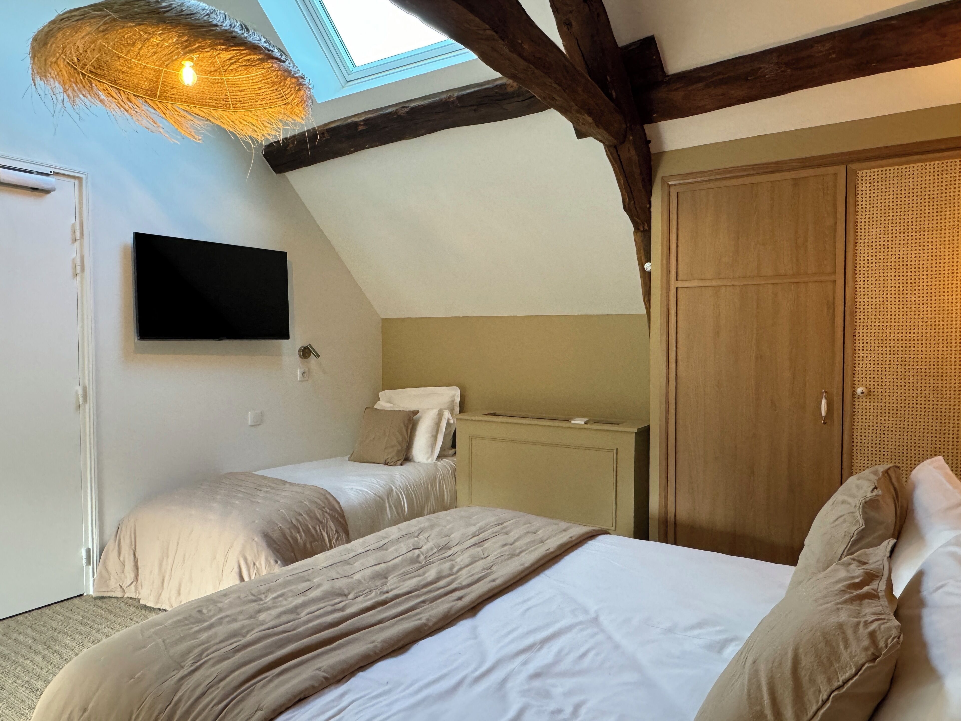 Une chambre avec deux lits, une télévision, une armoire et un puits de lumière.