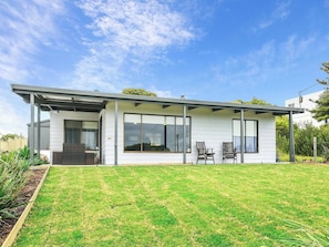 Une maison moderne de plain-pied, dotée de grandes fenêtres, d’un patio couvert et d’une pelouse bien entretenue.