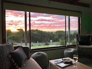 Une pièce avec une grande fenêtre, un canapé, un fauteuil et une table sur laquelle se trouve un verre de vin.