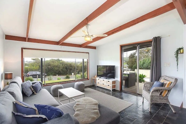 A spacious living room with a large TV, comfortable seating, and a view through a sliding glass door.