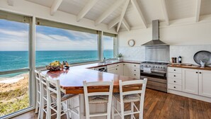 A kitchen with a view of the ocean, wooden flooring, white cabinets, and a large island with chairs. - Absolute Ocean Frontage 1 The Strand Pt Elliot (Port Elliot)