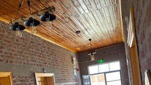 A room with exposed brick walls, wooden ceiling beams, and a large window with a view. - Moj Dom Küçükköy (Ayvalik)