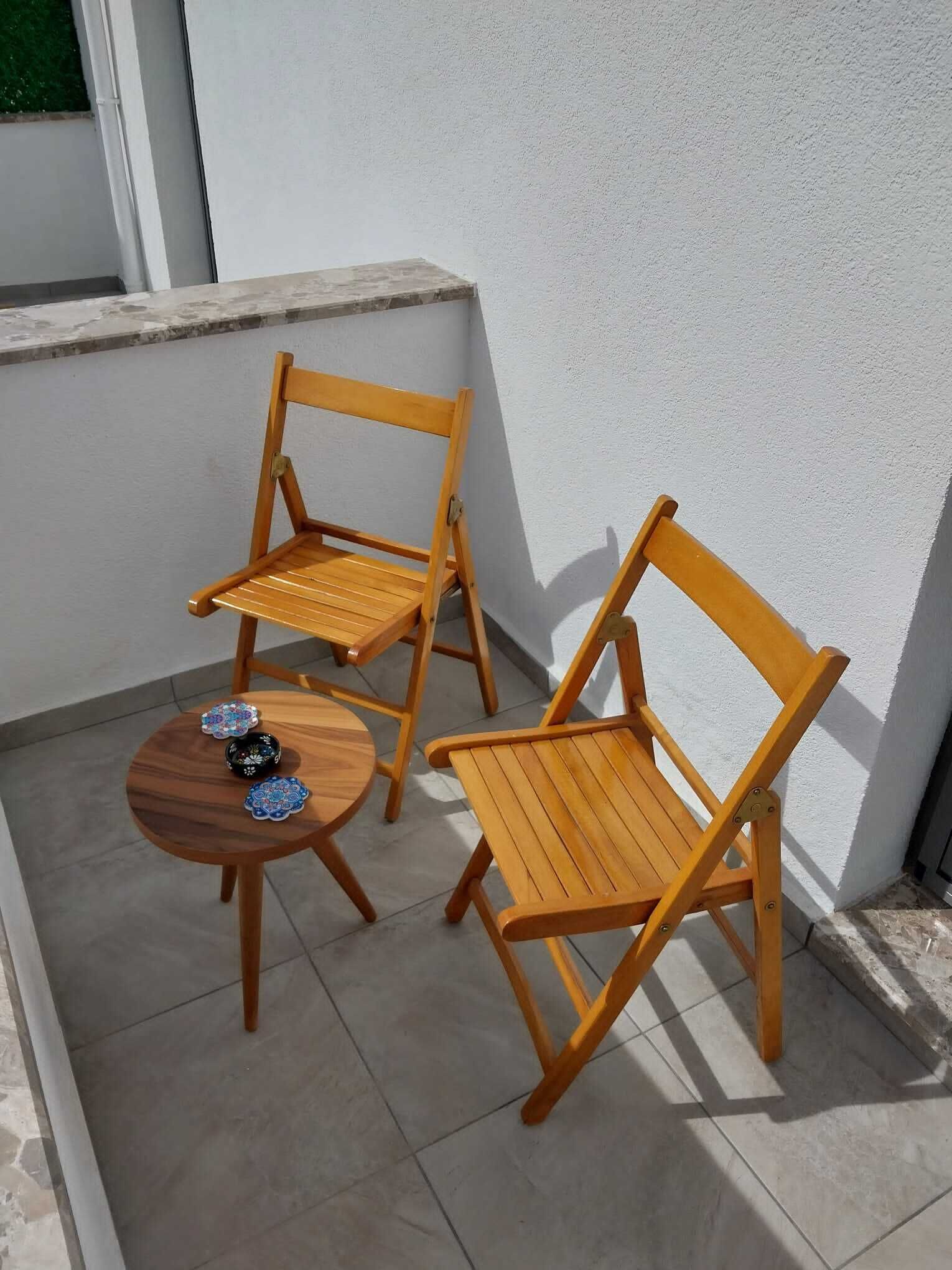 Two wooden chairs and a small round table with decorative plates on a tiled patio.