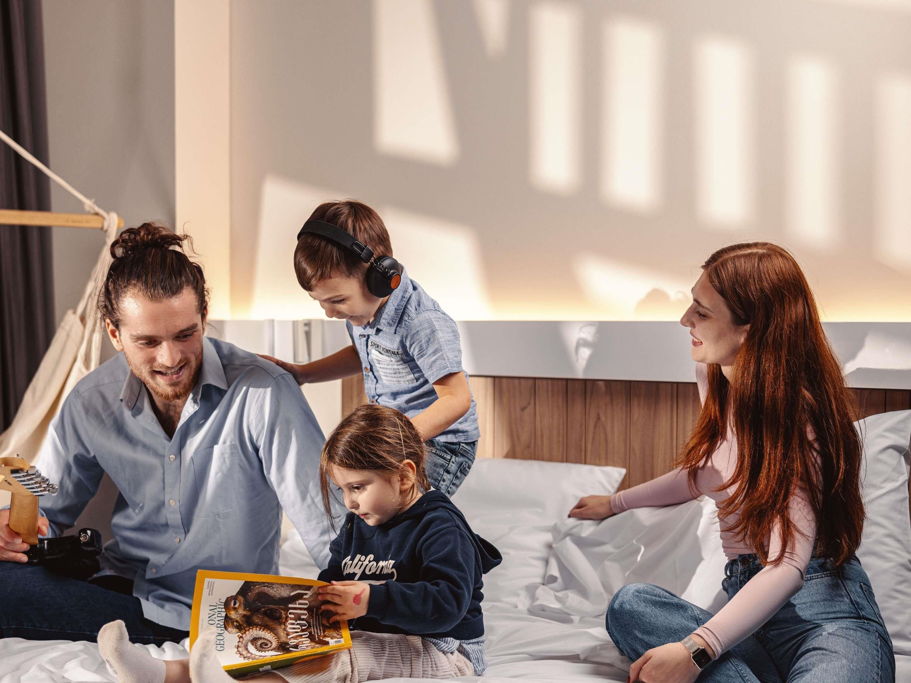 A family in a modern bedroom with a bed, a bedside table, and a wall-mounted shelf.
