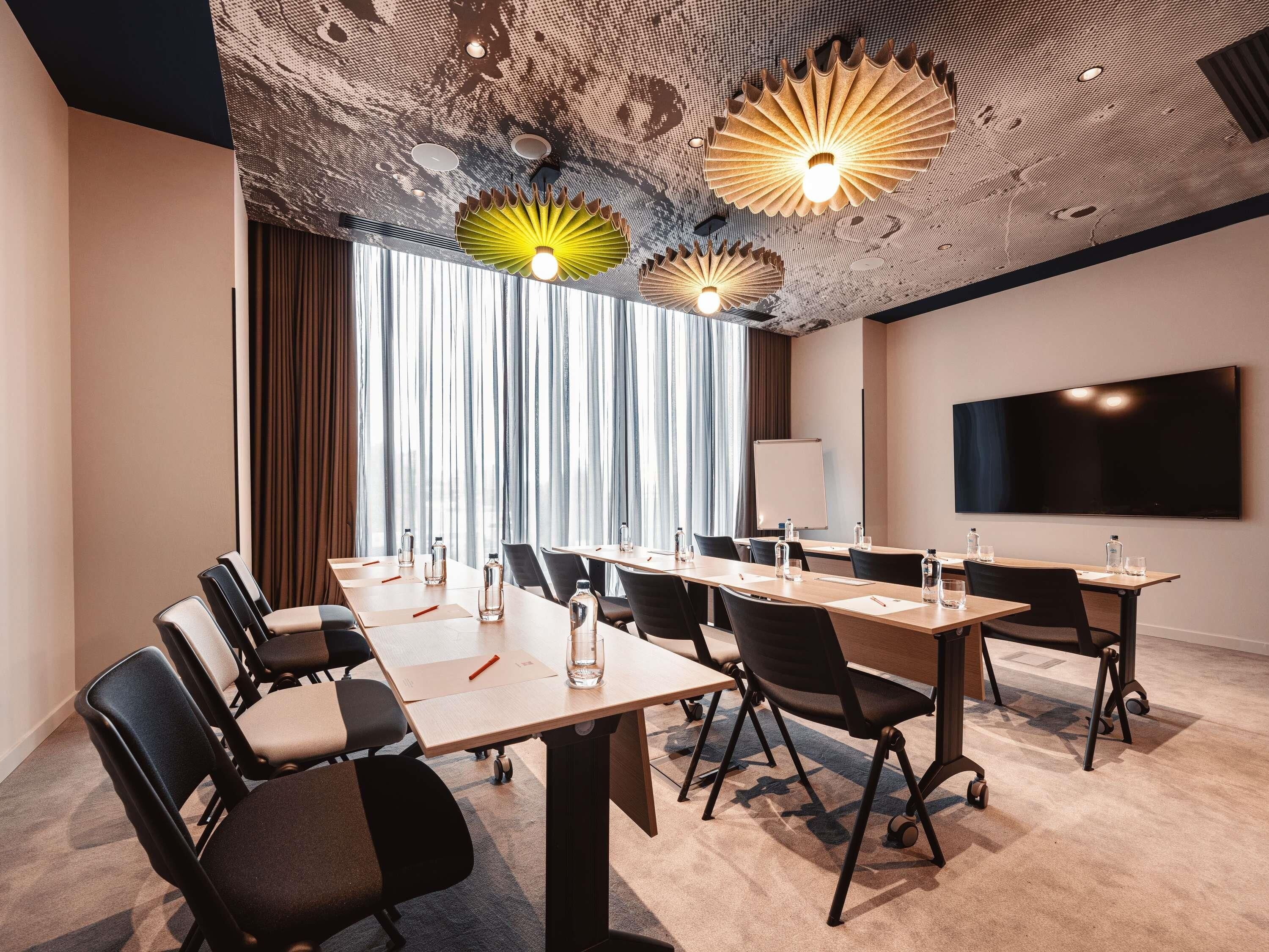 Une salle de conférence avec une longue table, des chaises, un tableau blanc et un téléviseur à écran plat fixé au mur.