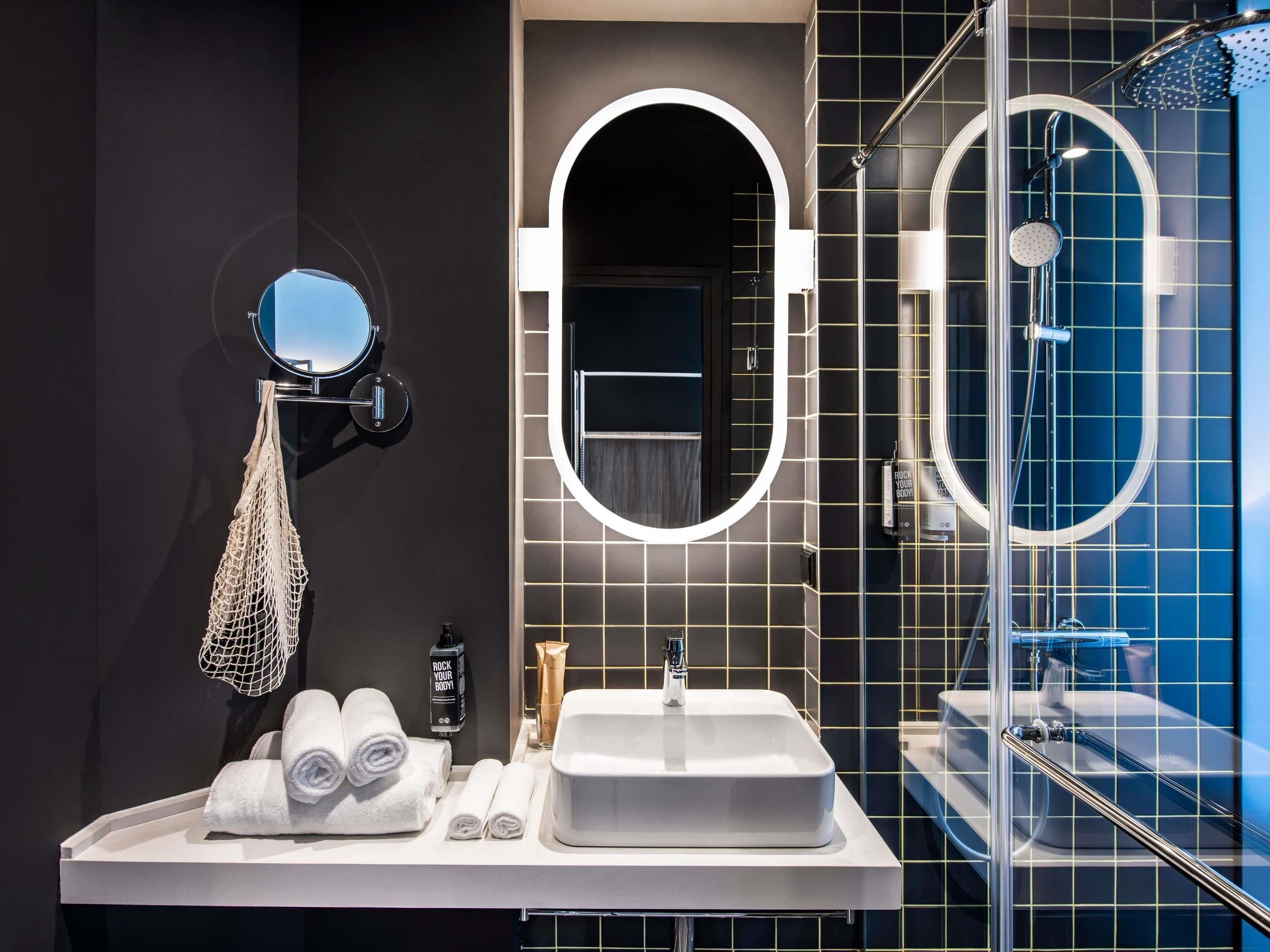 A modern bathroom with a white sink, a round mirror, a towel rack, and a shower area.