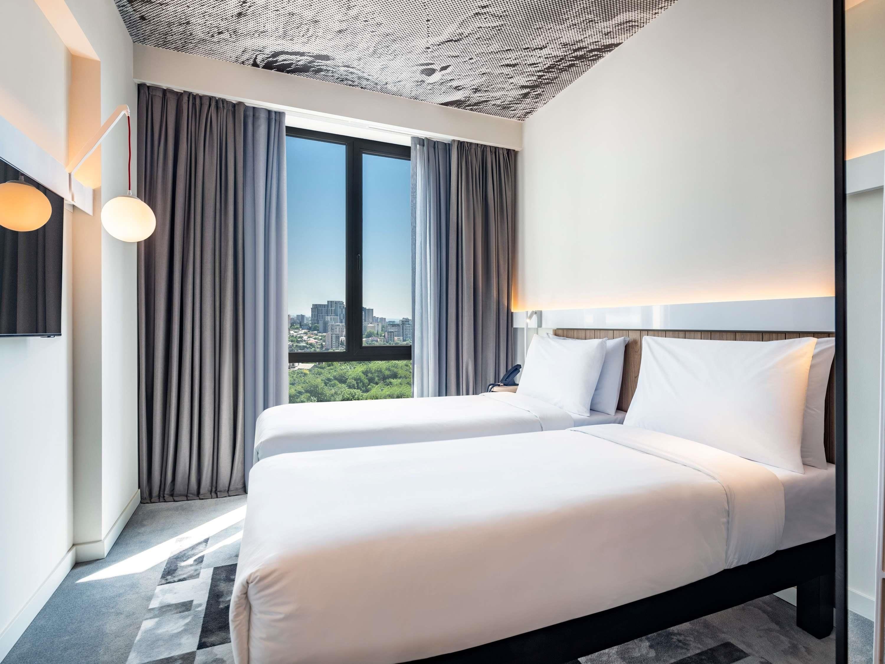 Una habitación de hotel moderna con dos camas, vistas a la ciudad y un techo estampado.