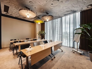 Un salón de conferencias con una mesa larga, sillas y una planta.