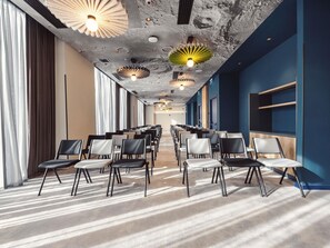 Una sala conferenze con file di sedie, un soffitto decorato e una parete azzurra.