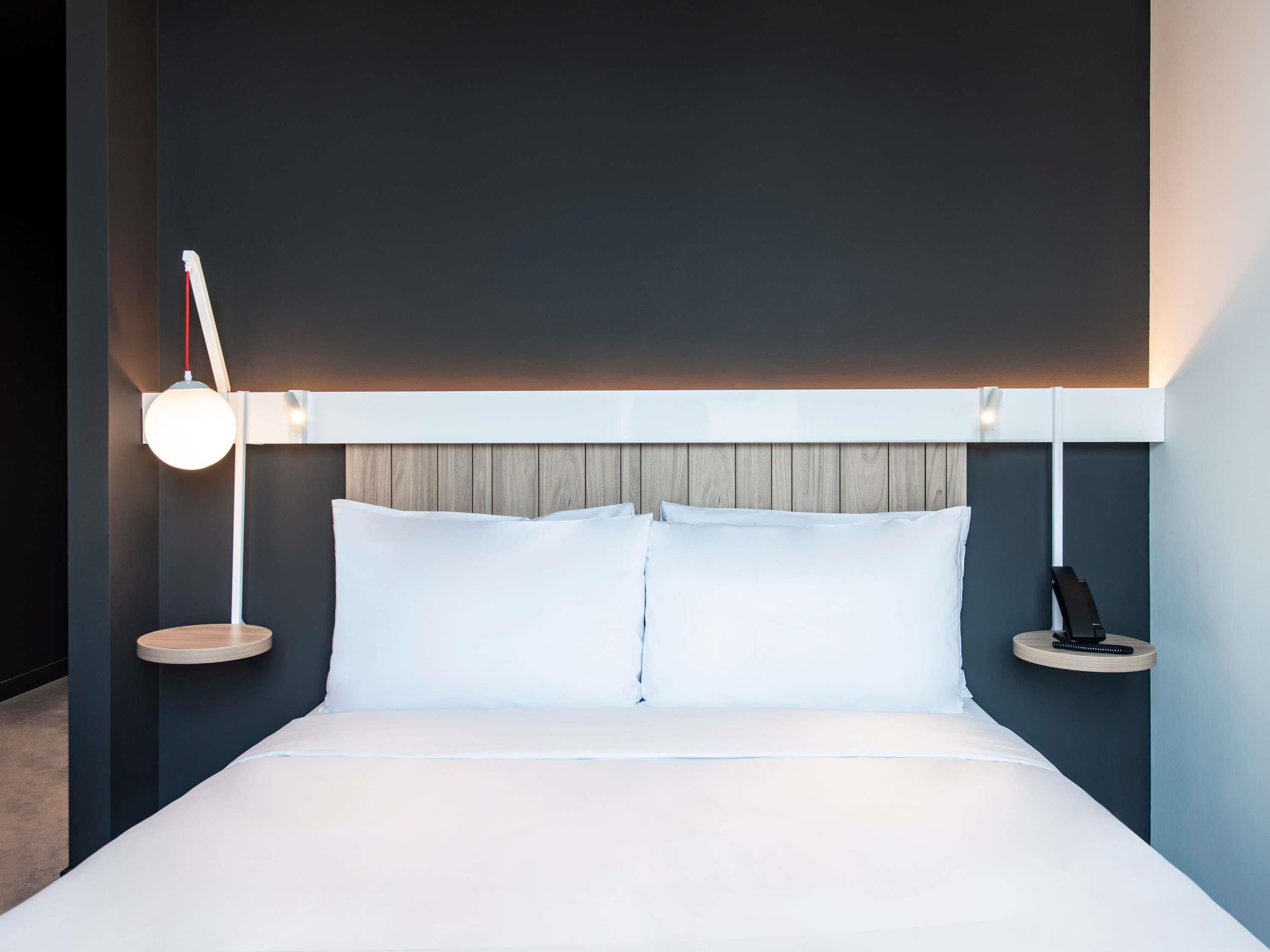 A modern hotel room with a large bed, a bedside lamp, a phone, and a small table.