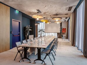 A conference room with a long table, chairs, a projector screen, and a large plant. - Ibis Tbilisi City (Tbilisi)