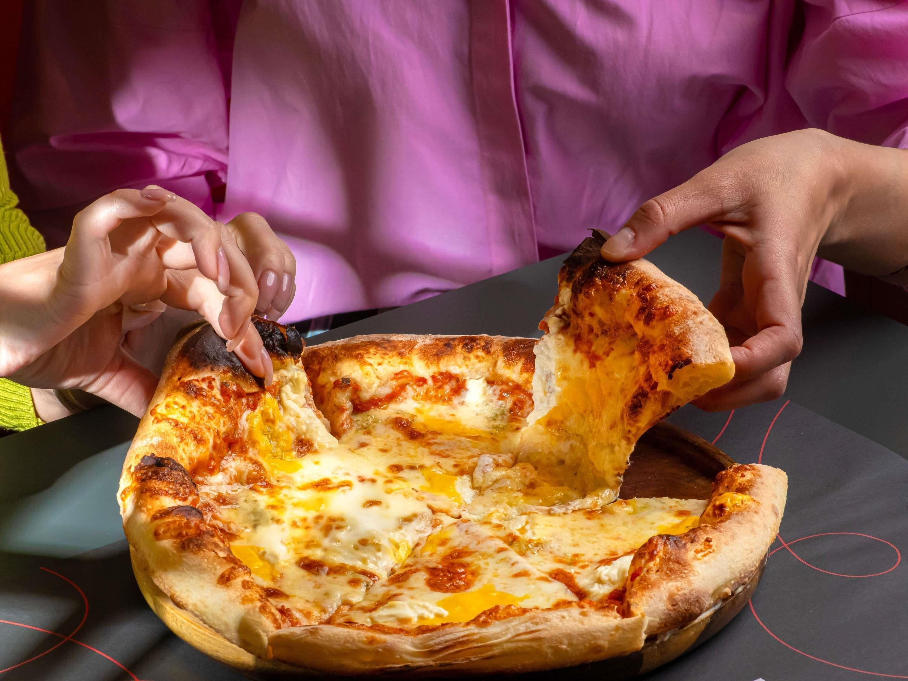 A person holding a slice of pizza with melted cheese and a charred crust.