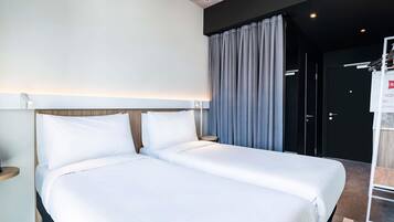 A hotel room with a double bed, a bedside table, a wall-mounted light, and a door leading to a bathroom.