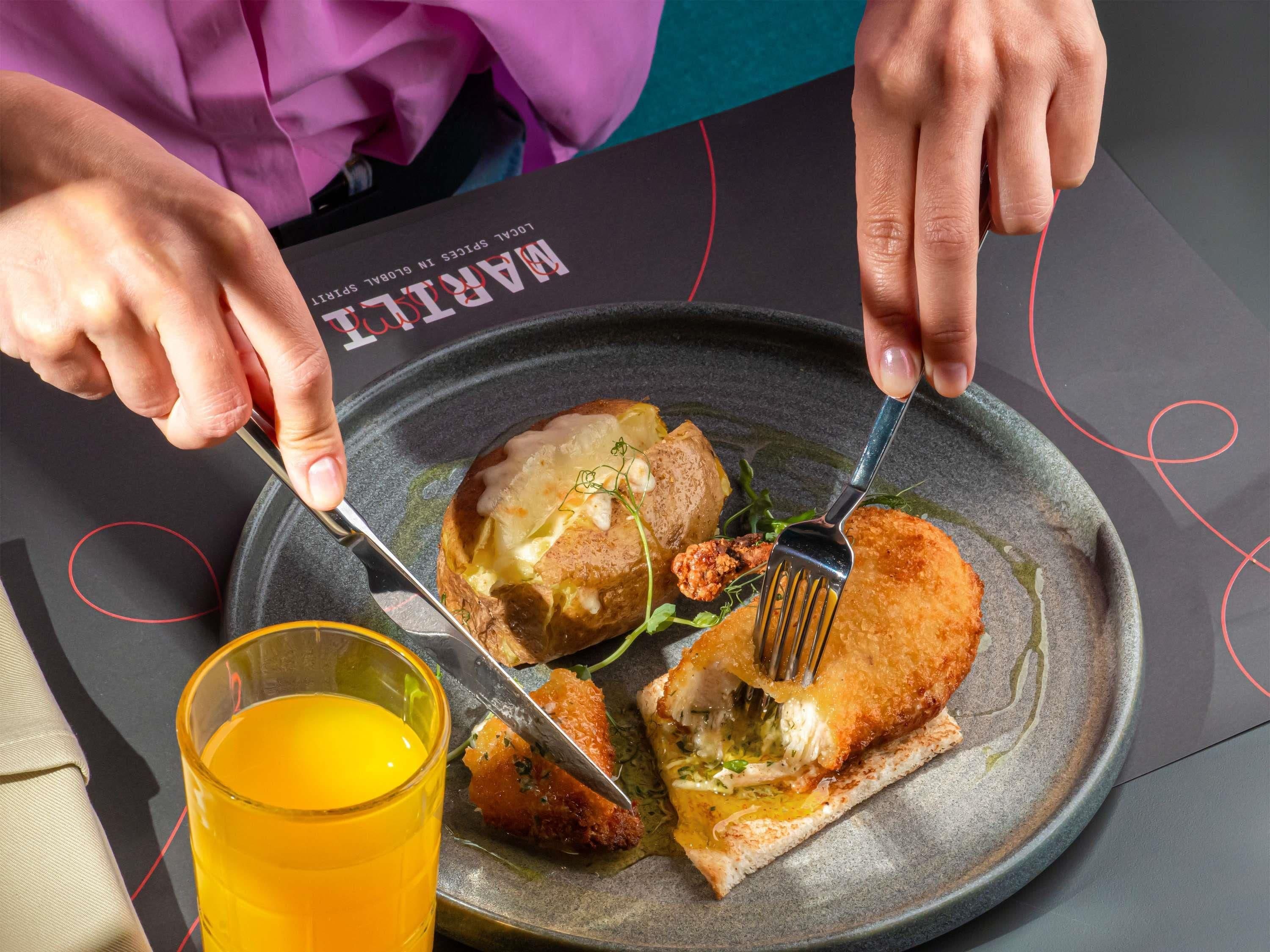 A person dining with a plate of food, a fork, and a glass of orange juice.