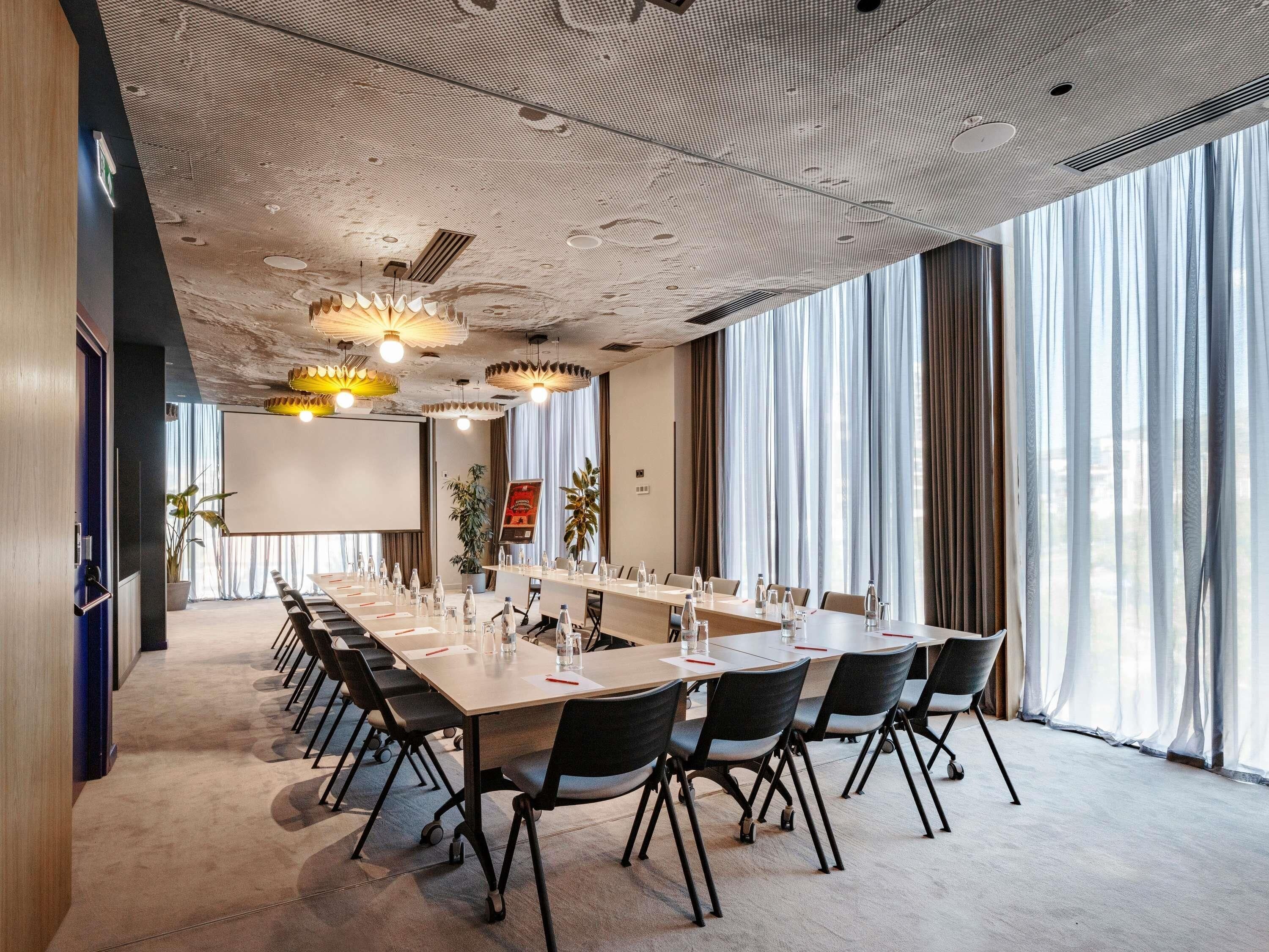 A conference room with a long table, chairs, and a projector screen.