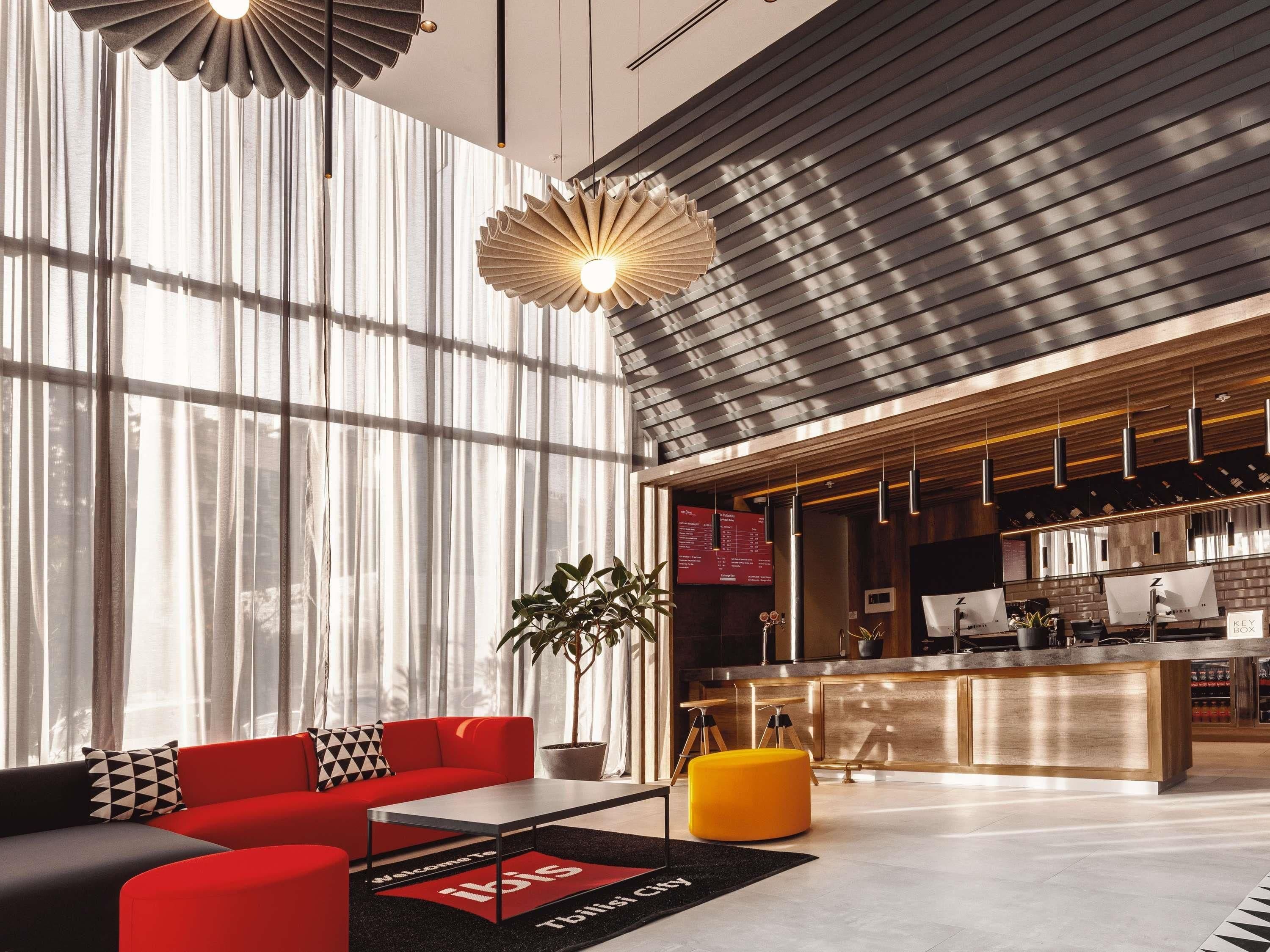 A modern hotel lobby with a red sofa, a coffee bar, and a large window with sheer curtains.